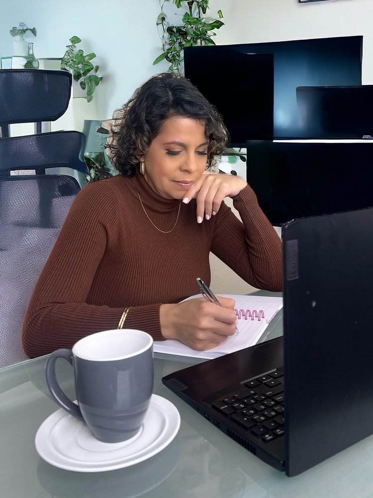 Maricruz Ascanio escribiendo en su cuaderno, pensativa, junto a una taza de café