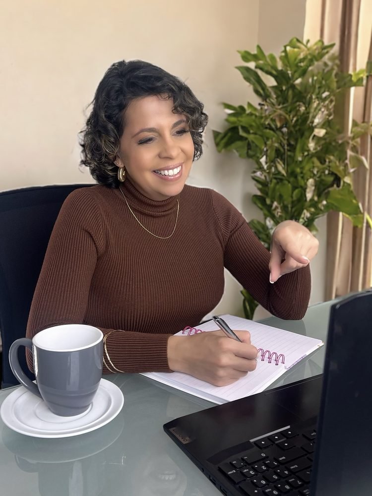 Maricruz Ascanio sonriendo en su escritorio, con cuaderno, café y laptop